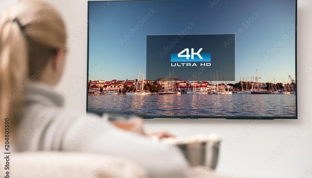 big modern tv with 4k resolutions and young woman on foreground watching some video