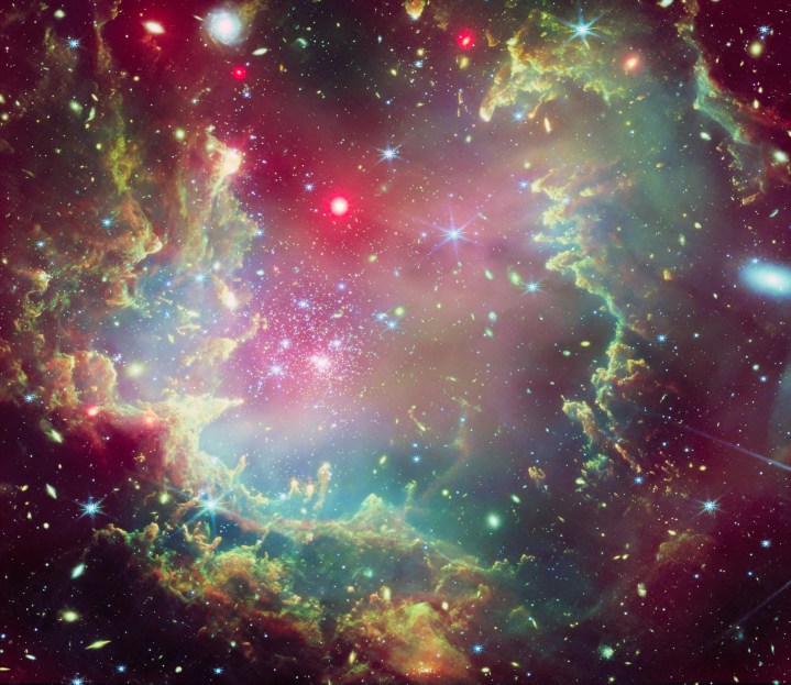 This image depicts star cluster NGC 602 in vibrant and festive colors, including a dust cloud ring resembling evergreen boughs. Red hints show X-ray shading, highlighting the layers within the ring.