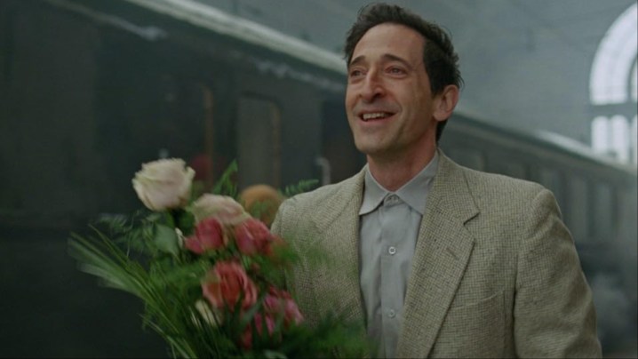 A man holds a bouquet of flowers in The Brutalist.