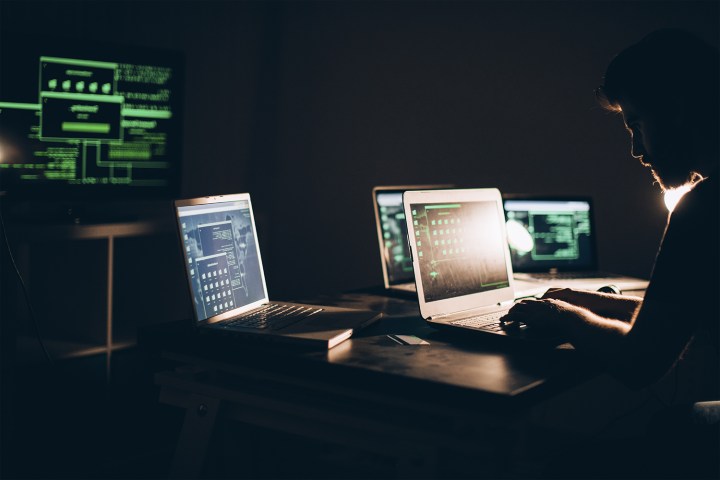 A person surrounded by multiple computers working on a laptop.