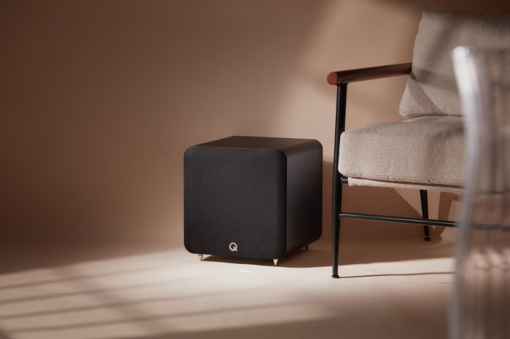 The Q Acoustics SUB100 subwoofer in black, placed next to a chair.