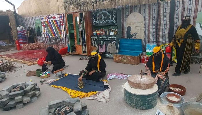 Women in traditional attire engage in historical household activities in Taif, Saudi Arabia.