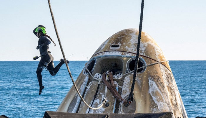 Support teams surround a SpaceX Dragon spacecraft shortly after it landed with NASA astronauts Nick Hague, Suni Williams, Butch Wilmore, and Russian cosmonaut Aleksandr Gorbunov.