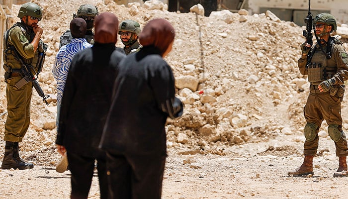 Israeli soldiers speak with a Palestinian woman outside Jenin camp during an Israeli military operation, July 8, 2025. — Reuters