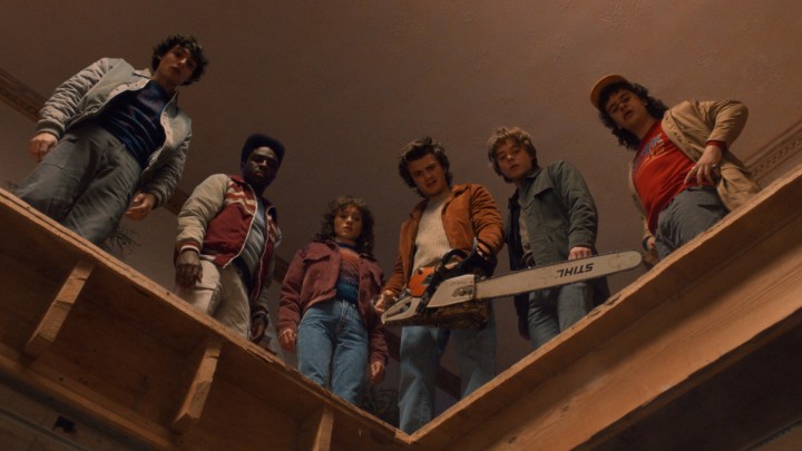 A group of teens look down as one holds a chainsaw.