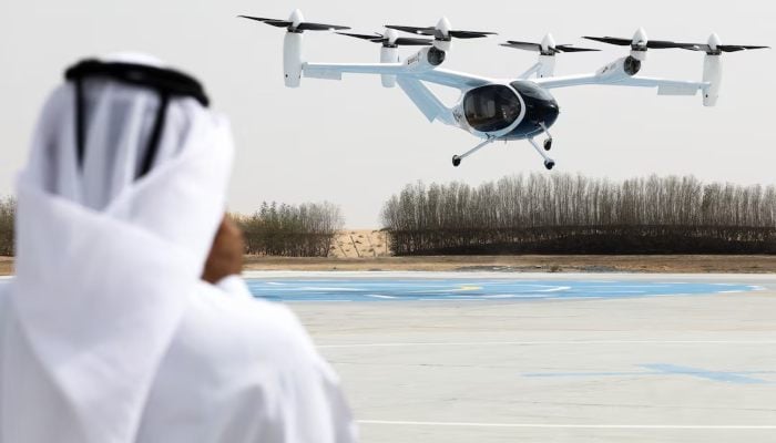 An individual in traditional Emirati attire captures footage of a test flight of an experimental Joby aerial taxi in Dubai, UAE, on June 30, 2025.