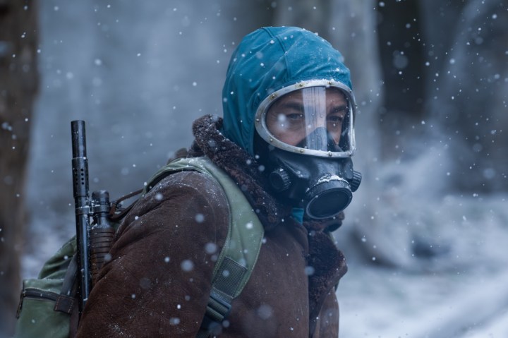 A man with a mask on stands in the snow.